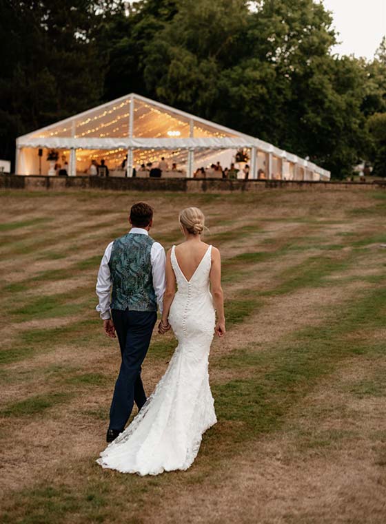 Bride and groom approach their beautiful illuminated frame marquee at dusk